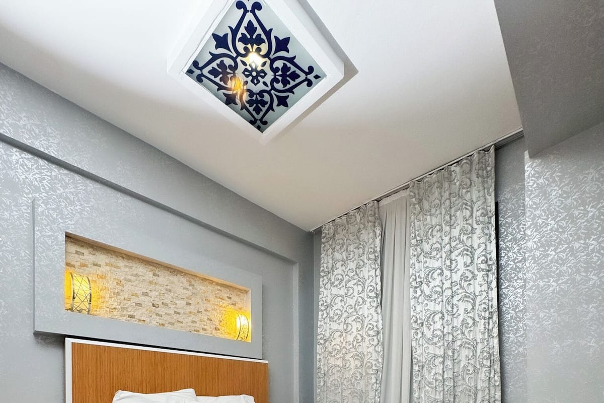A modern bedroom with a wooden bed, a nightstand, a decorative ceiling light, and patterned curtains.