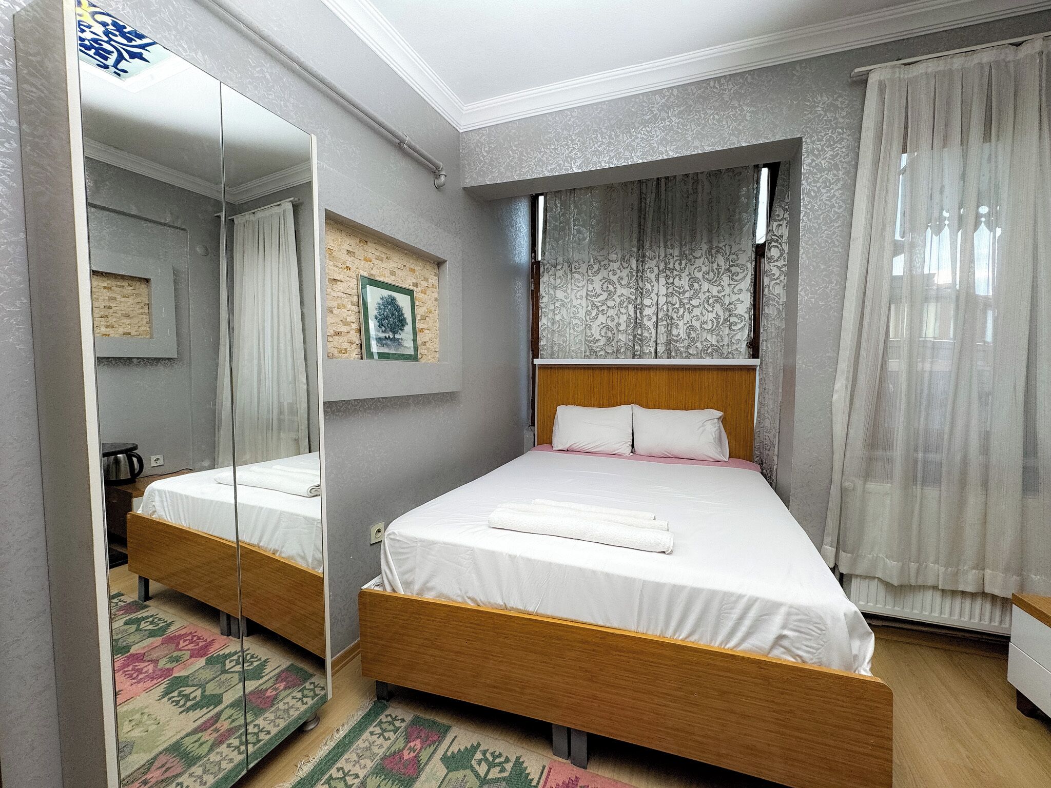 A double bed with a wooden headboard, a mirror, a picture frame, and a patterned rug.