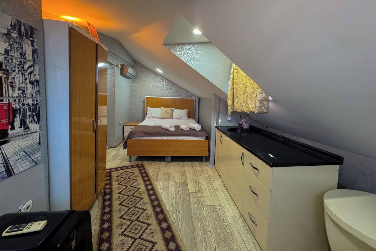 A compact bedroom with a bed, bedside table, and a small kitchenette.