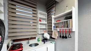 A modern kitchen with white cabinets, a red induction cooktop, a built-in sink, and a window with striped blinds. - The New Season Apart (Istanbul)
