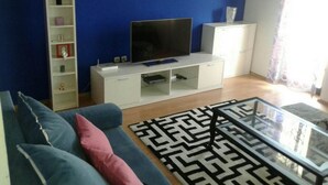 A living room with a sofa, a coffee table, a TV on a stand, a bookshelf, and a window with curtains. - Apartments Magda (Supetar)