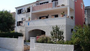 A two-story building with a balcony on the upper floor, a stone archway entrance, and potted plants on the balcony. - Apartments Magda (Supetar)