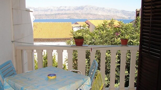 A balcony with a table and chairs, overlooking a mountainous landscape and a body of water. - Apartments Magda (Supetar)