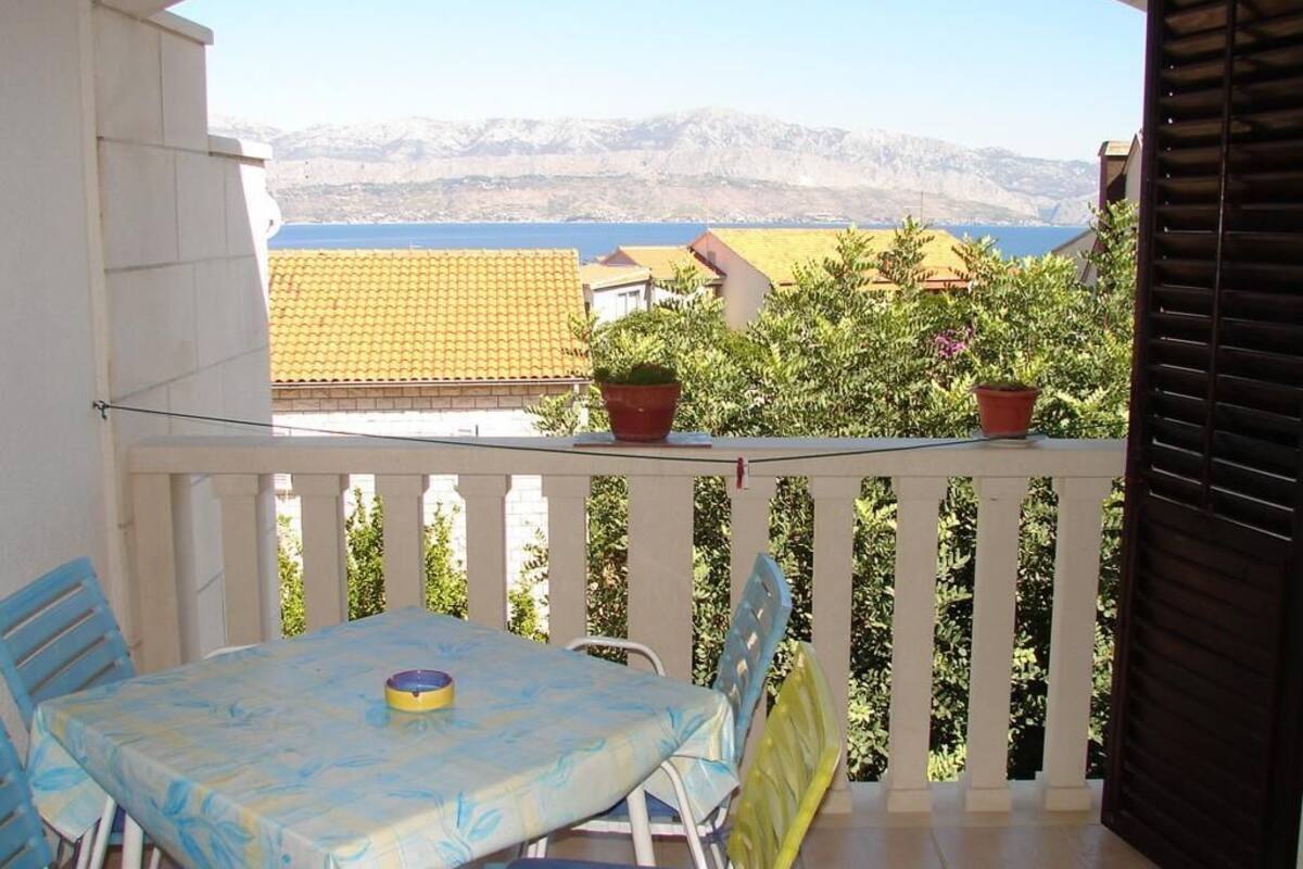 A balcony with a table and chairs, overlooking a mountainous landscape and a body of water.