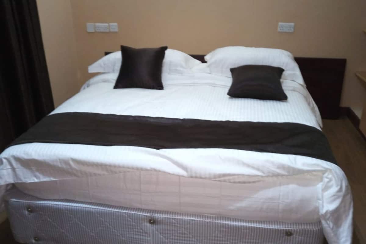 A neatly made bed with a white and dark brown bedspread, two pillows, and a dark headboard.