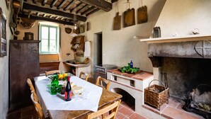 A rustic kitchen with a wooden table set for dining, a brick fireplace, and various kitchen utensils and decorations. - Villa Barsotti (Pescaglia)