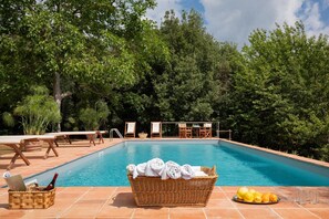 A swimming pool with lounge chairs and a wicker basket with towels and bottles.