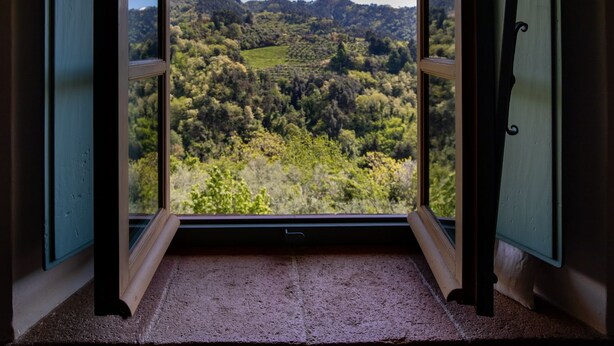 A room with a large window offering a view of a green landscape with hills. - Villa Barsotti (Pescaglia)