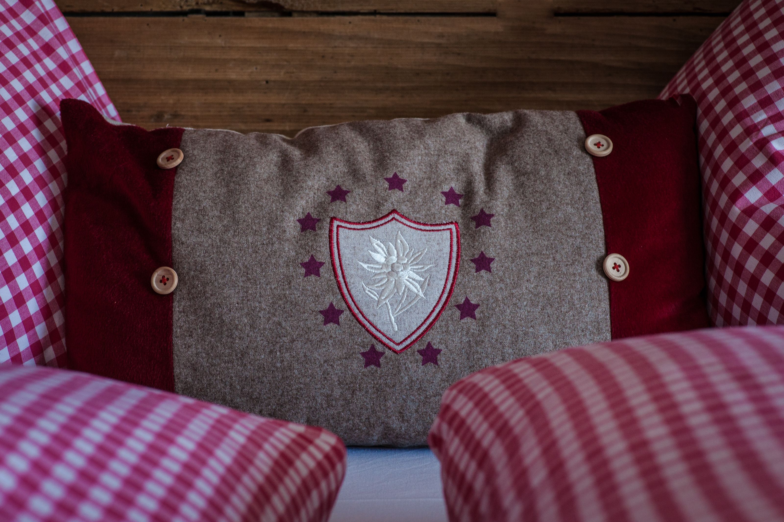 Un almohadón con escudo y estrellas, colocado entre almohadones cuadriculados sobre una cama.