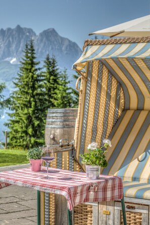 A cozy outdoor seating area with a striped cushion, a table with a checkered tablecloth, a wine glass, and a potted plant. - Angerer Alm (Sankt Johann in Tirol)