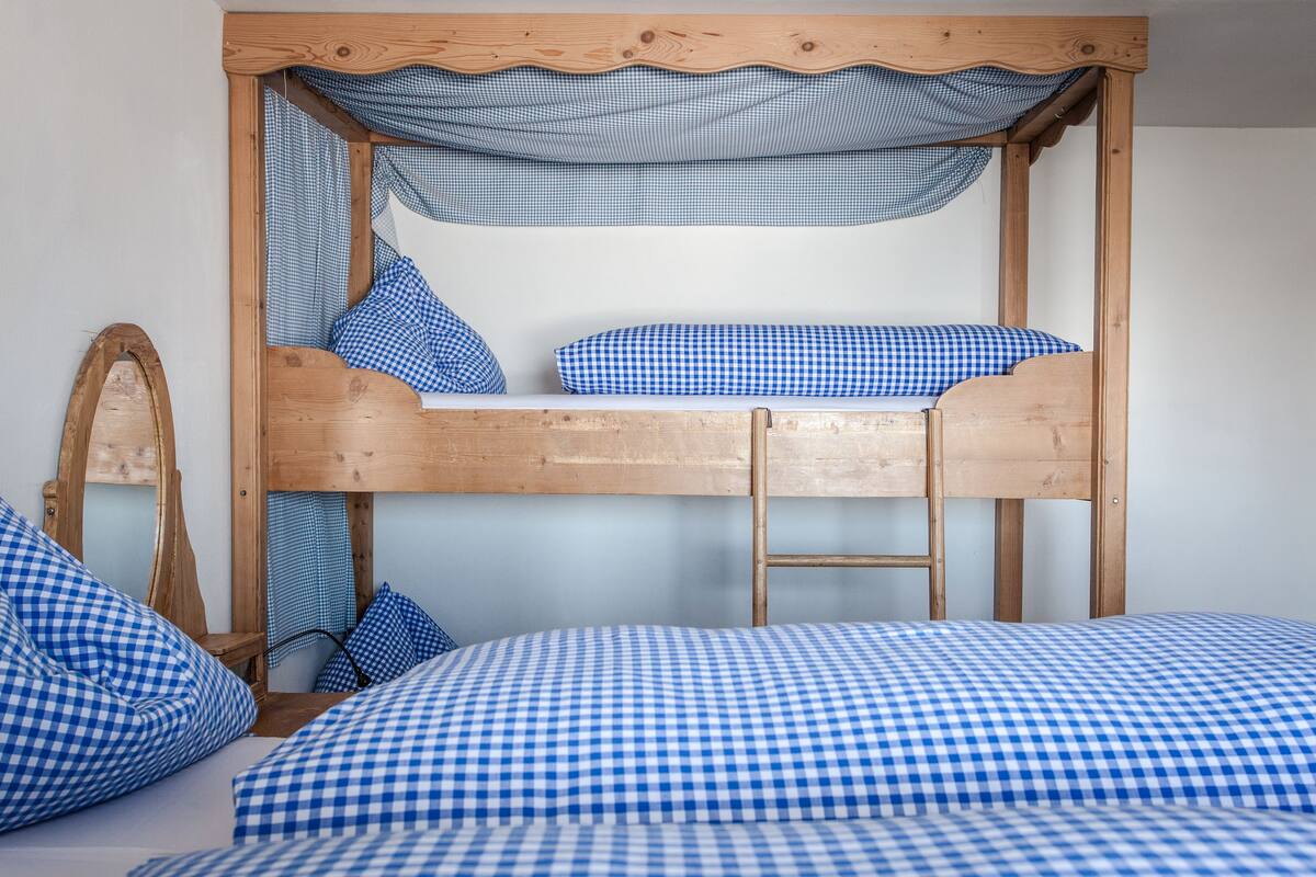 A bunk bed with a wooden frame, checkered bedding, and a ladder.