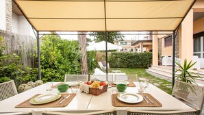 Un espace repas avec une table dressée pour quatre personnes, entourée de chaises, sous une tonnelle.