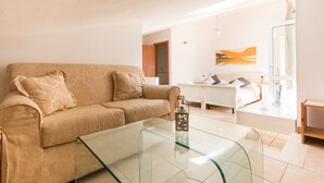 Un salon moderne avec un canapé beige, une table basse en verre et un bureau blanc à l’arrière-plan.