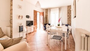 Un salon bien éclairé, équipé d’un téléviseur, d’un livre d’or et d’un coin repas avec une table et des chaises.