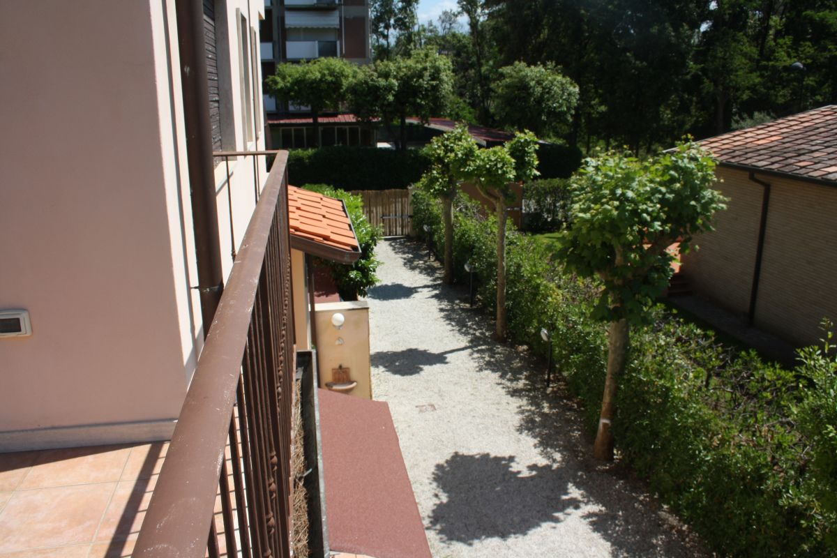 Un sendero estrecho bordeado por edificios y vegetación, que conduce a una zona cubierta con tejado de baldosas.