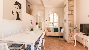 Un salon moderne avec un canapé blanc, une table à manger avec des chaises, un téléviseur posé sur un meuble et un mur d’accent en pierre.