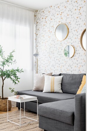 A modern living room with a grey sofa, white side table, and a potted plant. - Go Madrid Apartments by Olala Homes (Madrid)