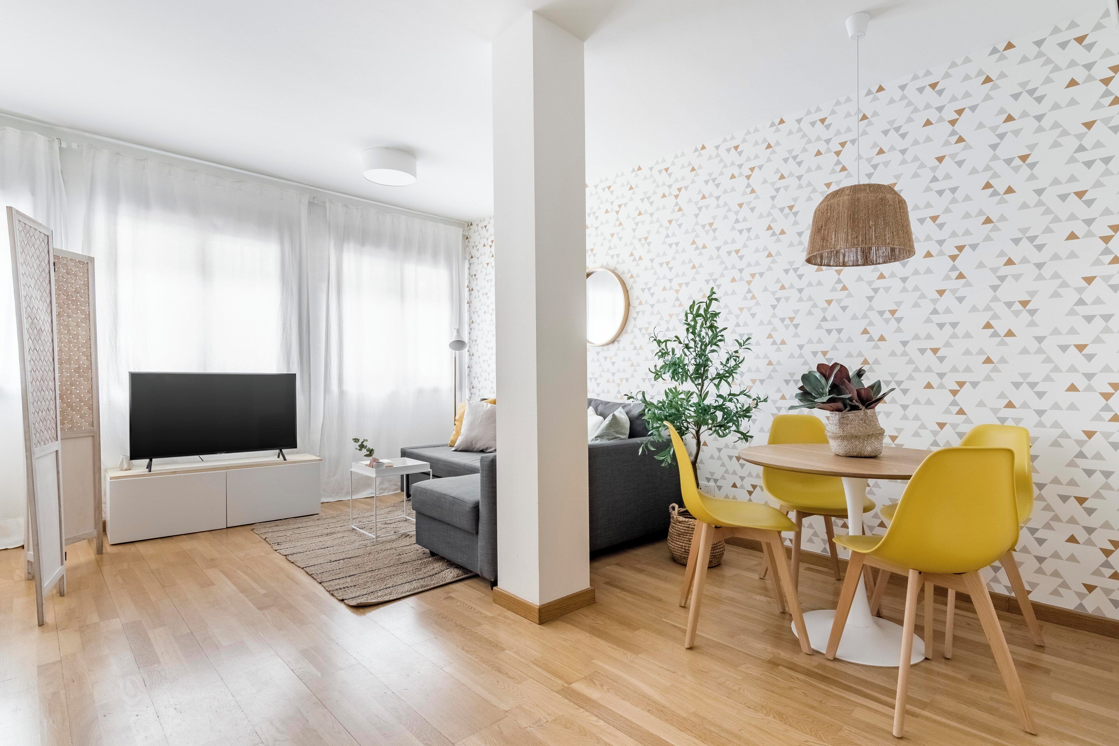 Ein modernes Wohnzimmer mit Flachbildfernseher, grauem Sofa, gelben Sesseln und einem Esstisch.