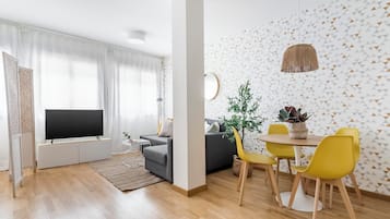 Una sala de estar moderna con televisor de pantalla plana, sofá gris, sillas amarillas y una mesa de comedor.