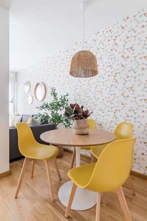 A dining area with a round wooden table, yellow chairs, a hanging light fixture, and a patterned wall. - Go Madrid Apartments by Olala Homes (Madrid)