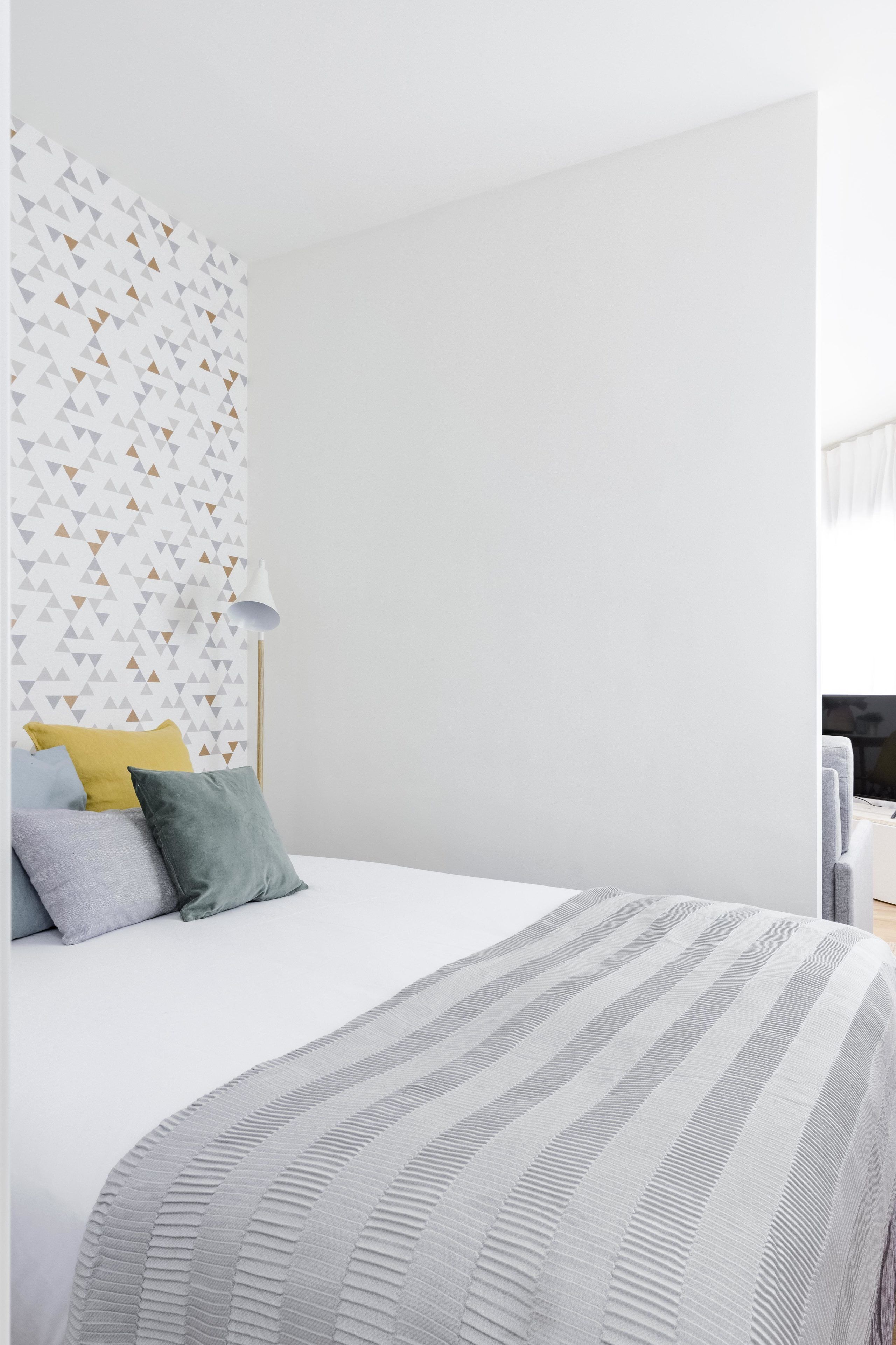 A modern bedroom with a white bed, a geometric-patterned wall, and a striped area rug.