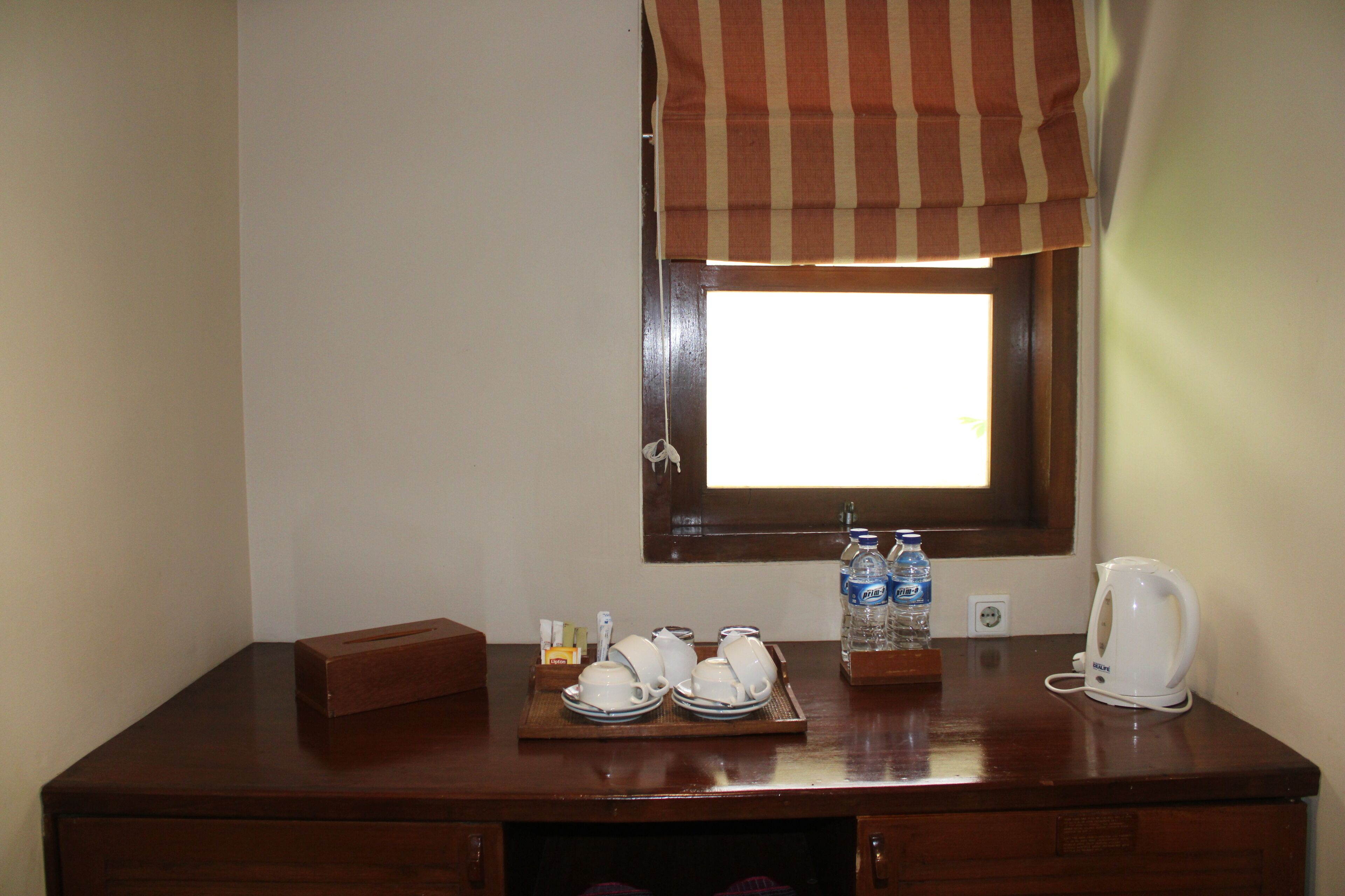 A wooden desk with a tray of white cups and saucers, a white electric kettle, and two bottles of water.