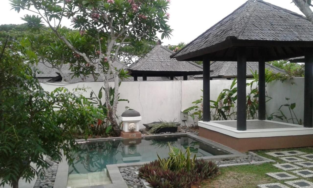 A serene garden with a small pool, surrounded by lush greenery and two thatched-roof structures.