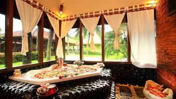 Unwind in a serene spa room with a spacious oval bathtub and lush greenery views through large windows.