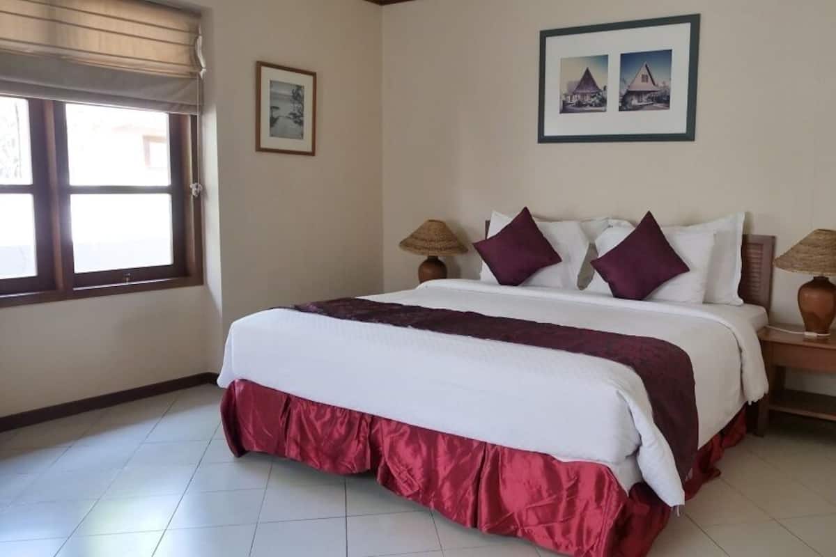 Une chambre d’hôtel avec un grand lit, deux lampes de chevet, une fenêtre avec des stores et un tableau encadré au mur.