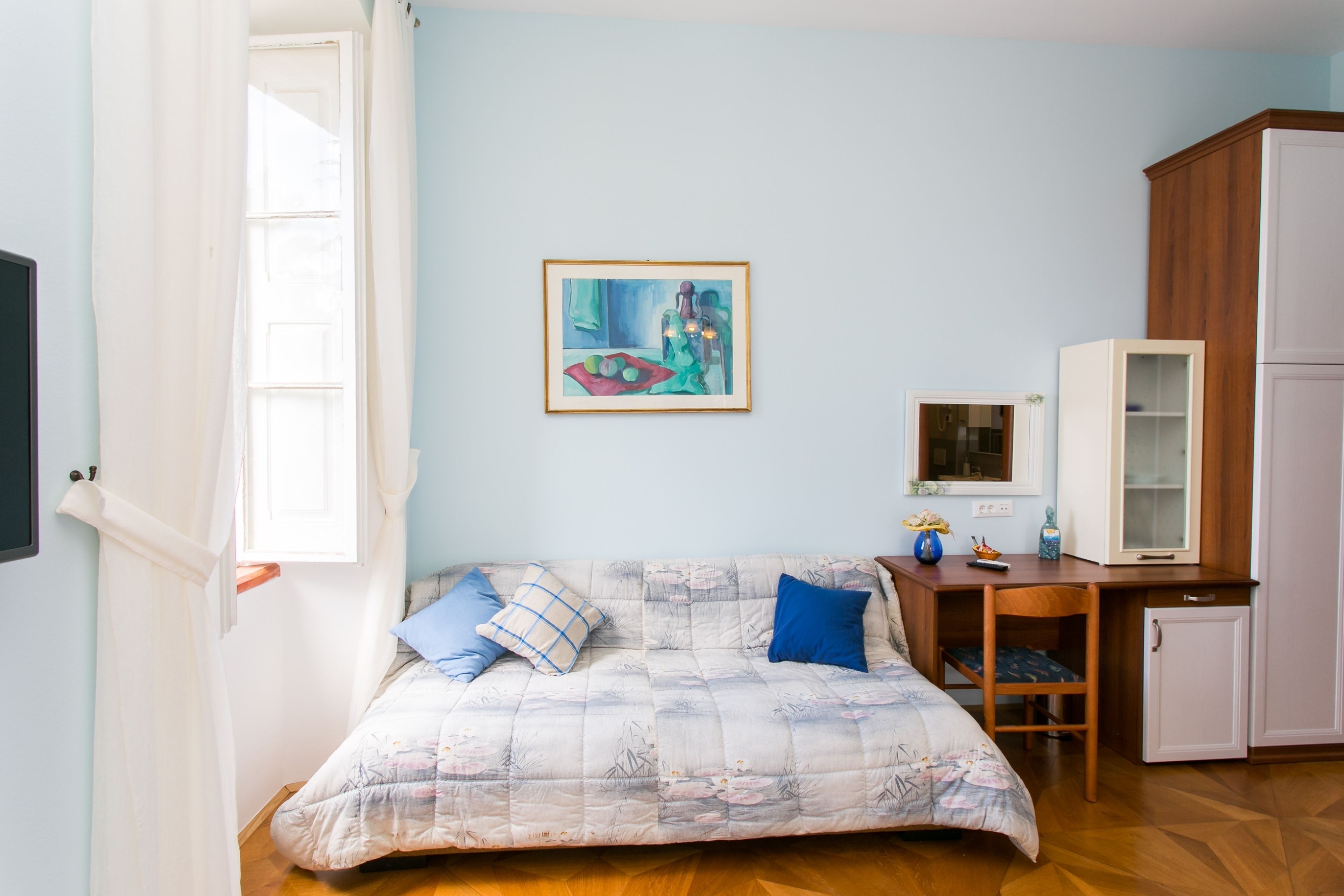 A bedroom with a bed, a desk, a cabinet, and a painting on the wall.