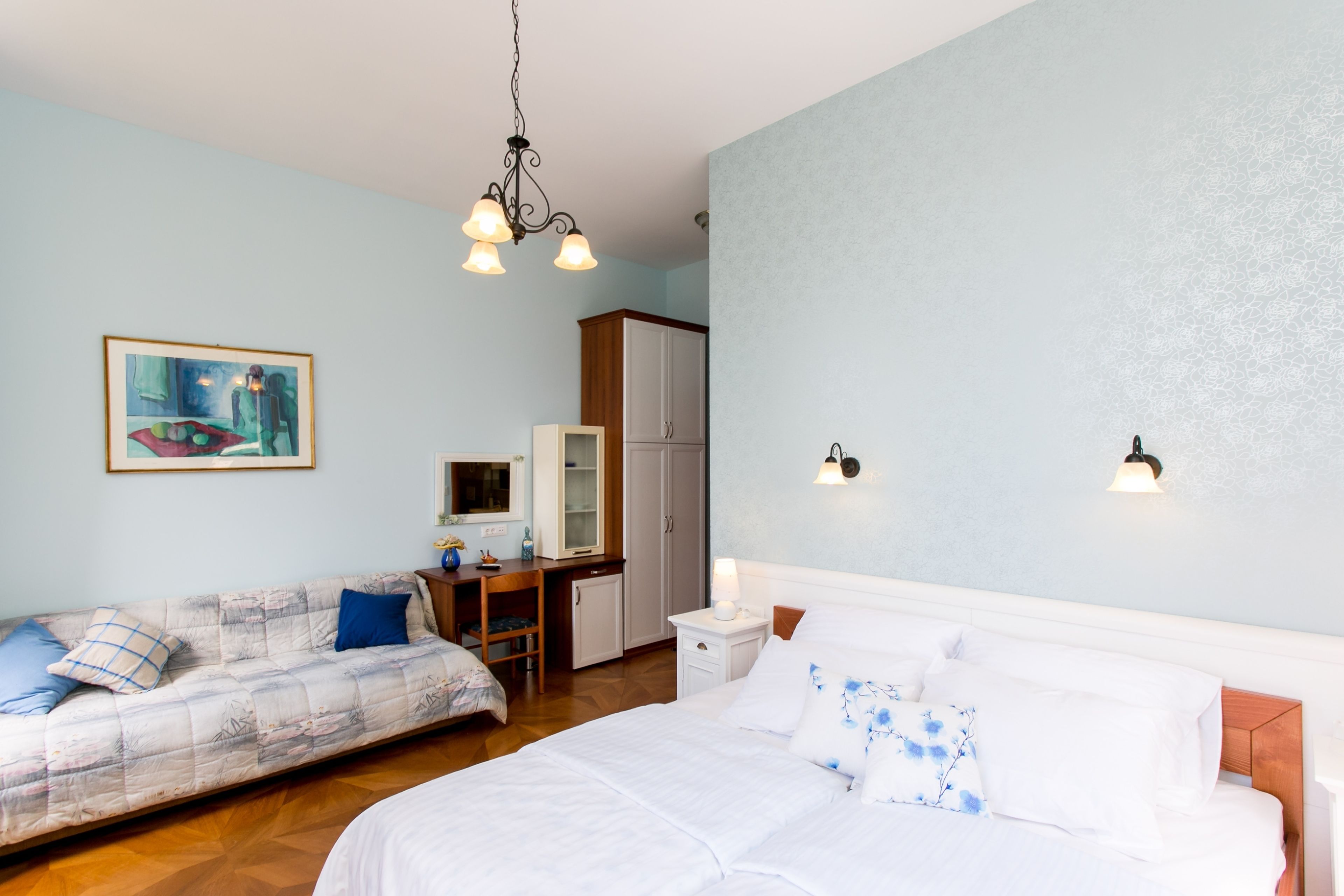 A bedroom with a bed, a sofa, a desk, and a wardrobe.