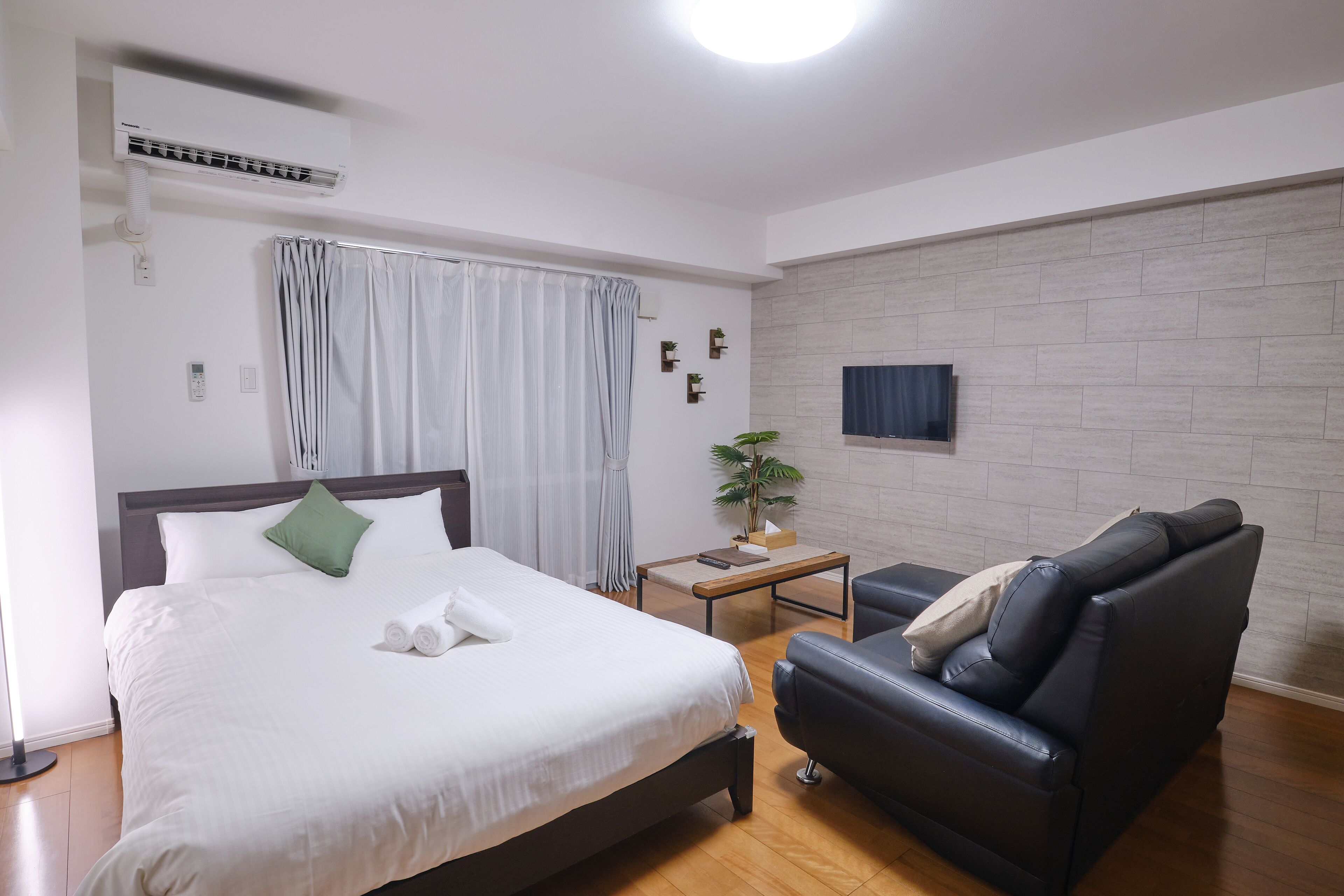 A hotel room with a bed, a sofa, a small table, and a wall-mounted TV.