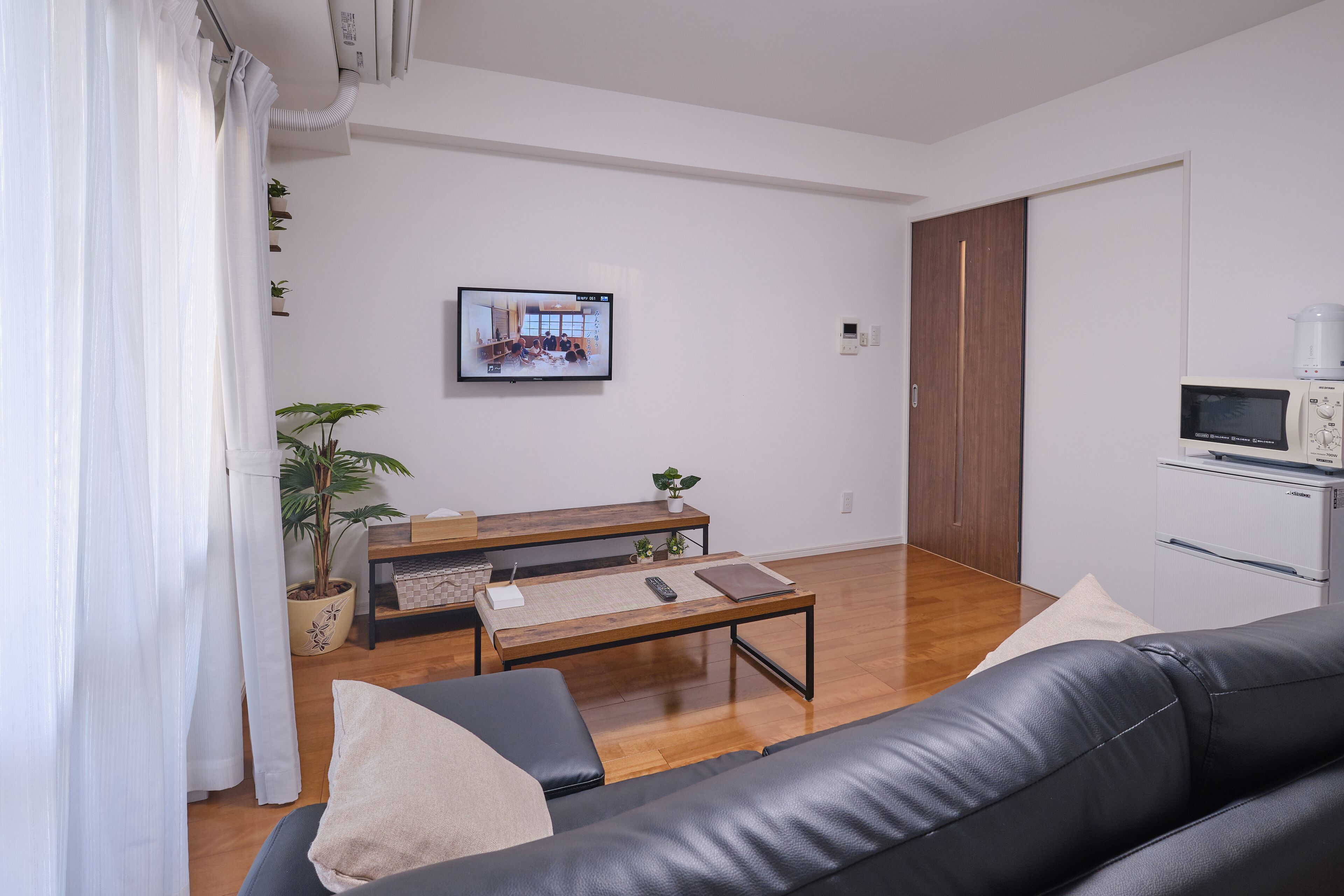 Een moderne woonkamer met een zwarte leren bank, een houten salontafel en een televisie aan de muur.