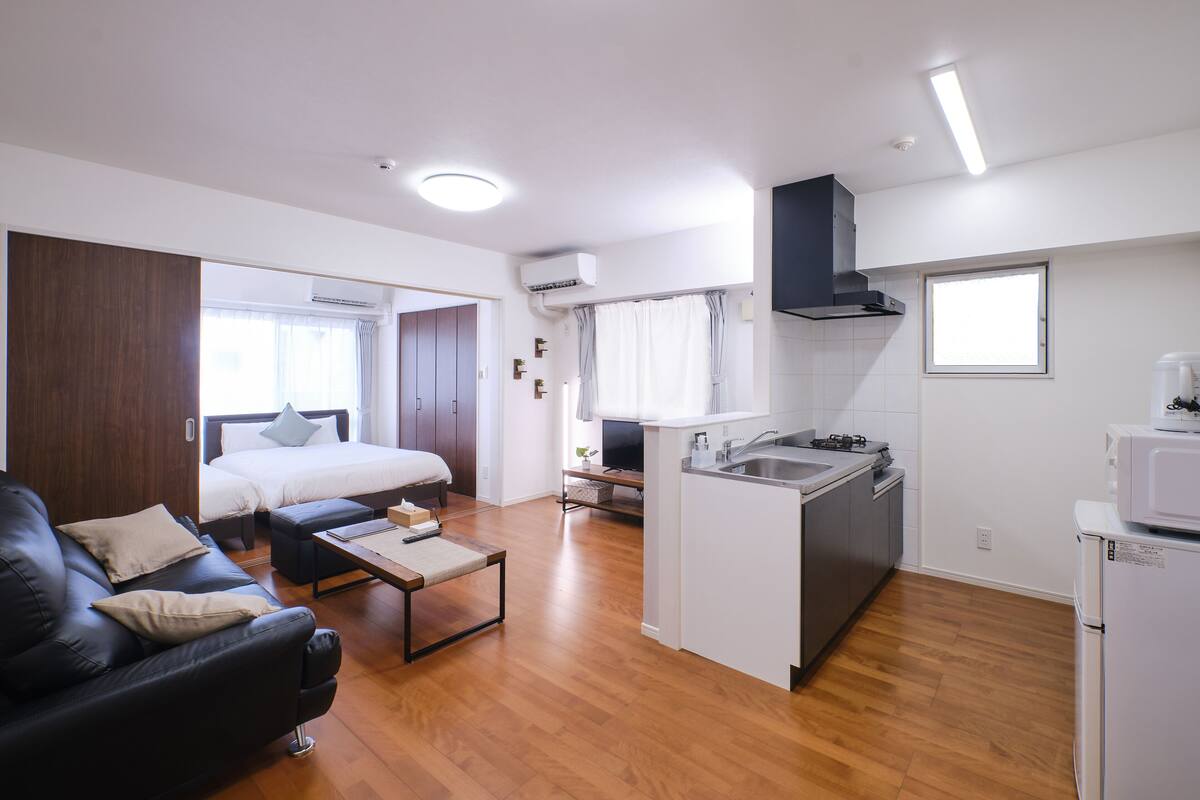 Un espacio habitable compacto con kitchenette, una cama, un sofá y una pequeña zona de comedor.