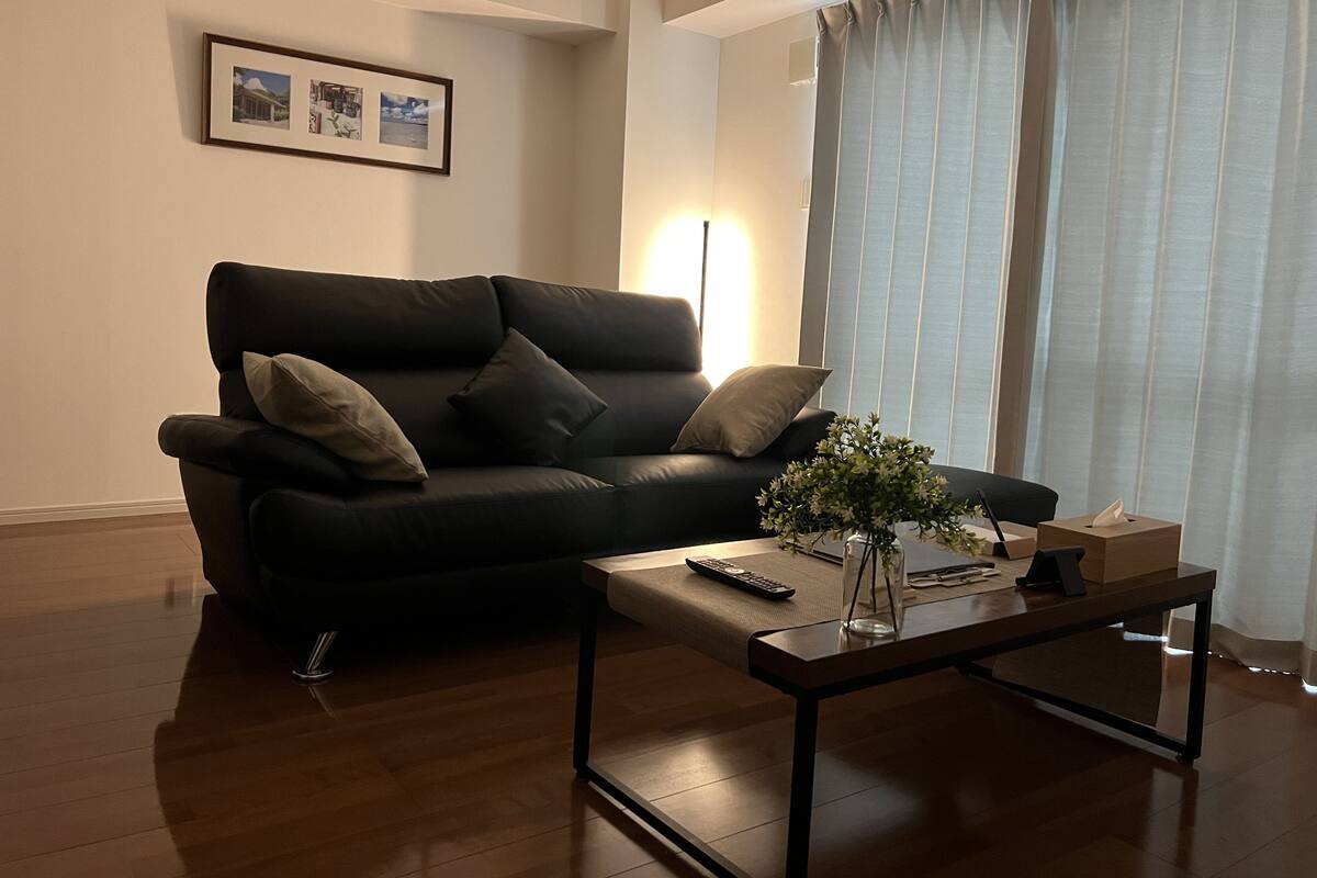 Una sala de estar con un sofá negro, una mesa de centro y un cuadro en la pared.