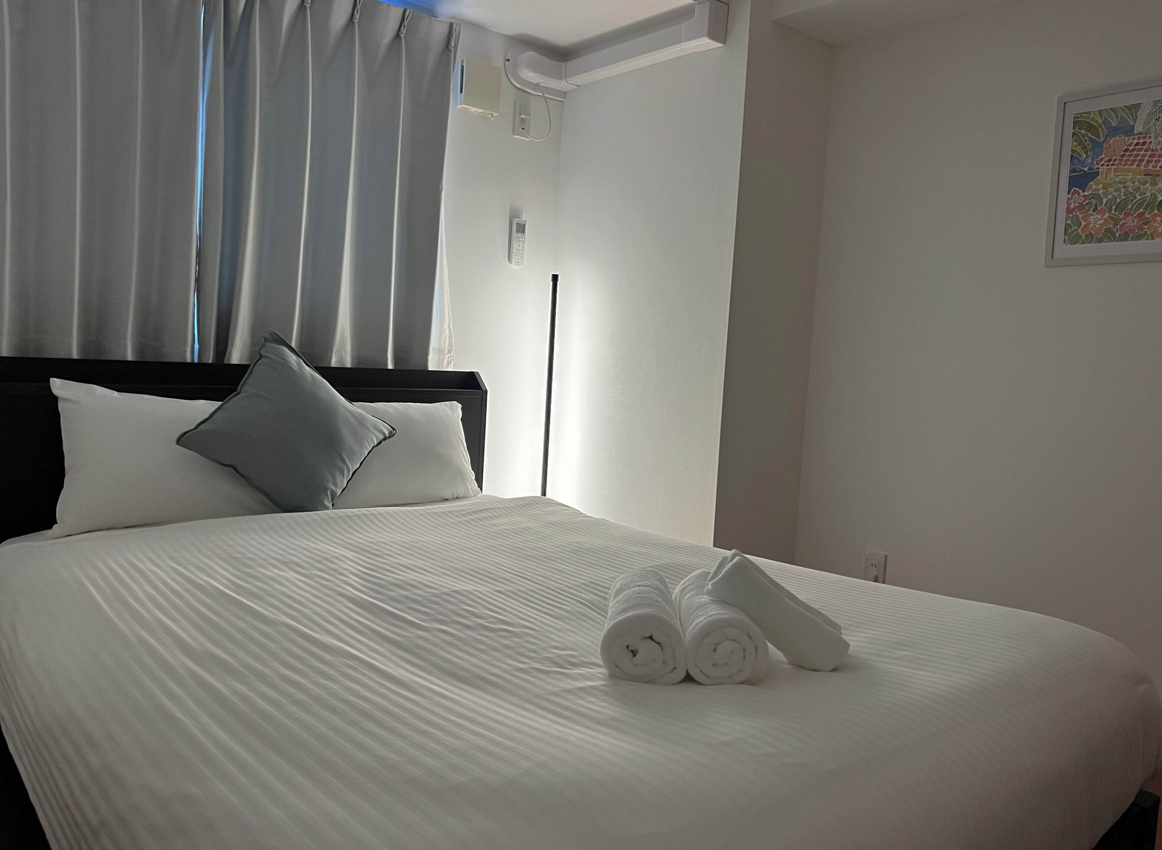 Una cama bien hecha con sábanas blancas, un cabecero negro y una sola almohada.