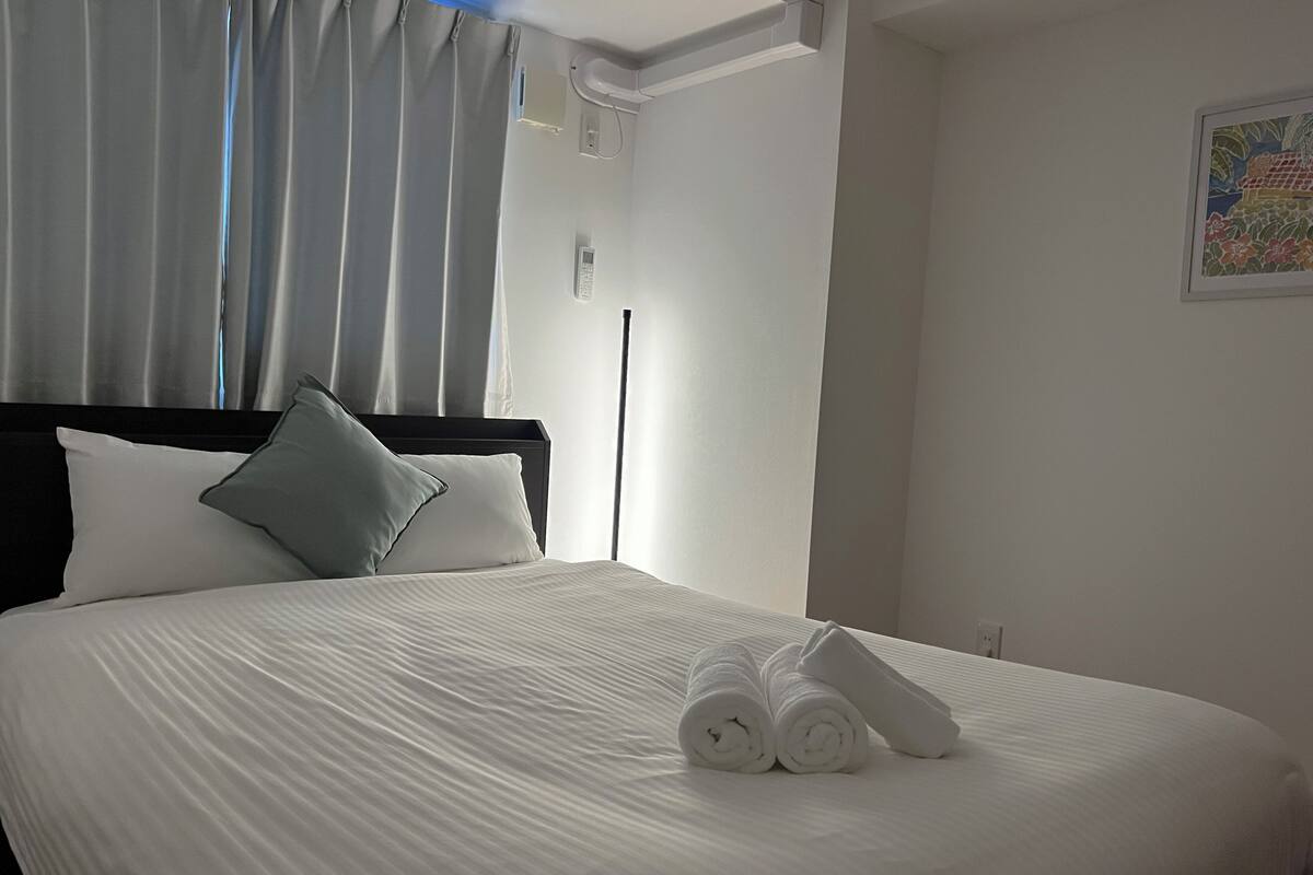 Una cama bien hecha con sábanas blancas, un cabecero negro y una sola almohada.