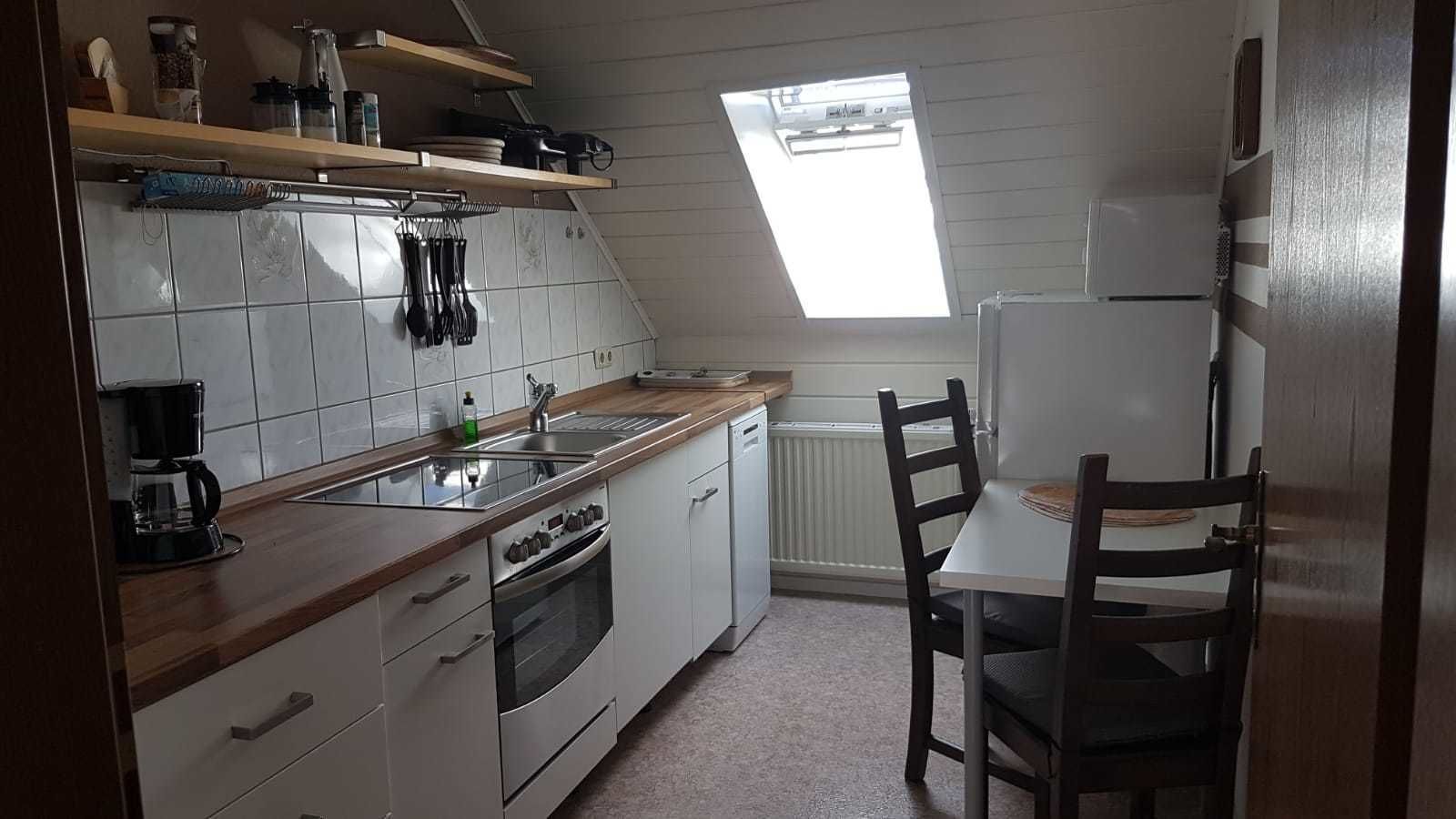 Una cucina compatta con mobili bianchi, un piano di lavoro in legno, forno integrato, lavello e una finestra sopra il termosifone.