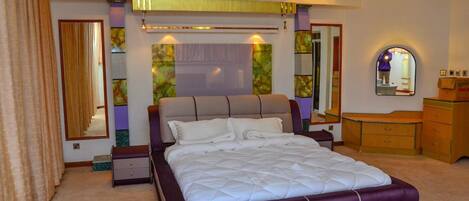 A bedroom with a large bed, a dresser, a mirror, and a carpeted floor.