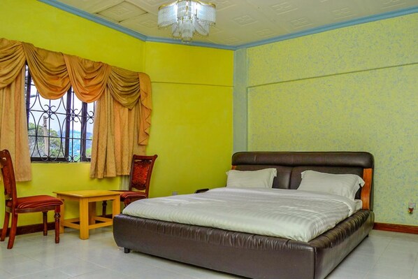 Un dormitorio con una cama grande, una silla de madera, una mesita y una ventana con cortinas.