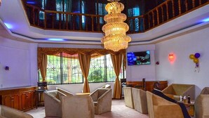 Ein geräumiger Lounge-Bereich mit gestuften Sitzplätzen, einer großen Kronleuchter und einem Fernsehbildschirm.