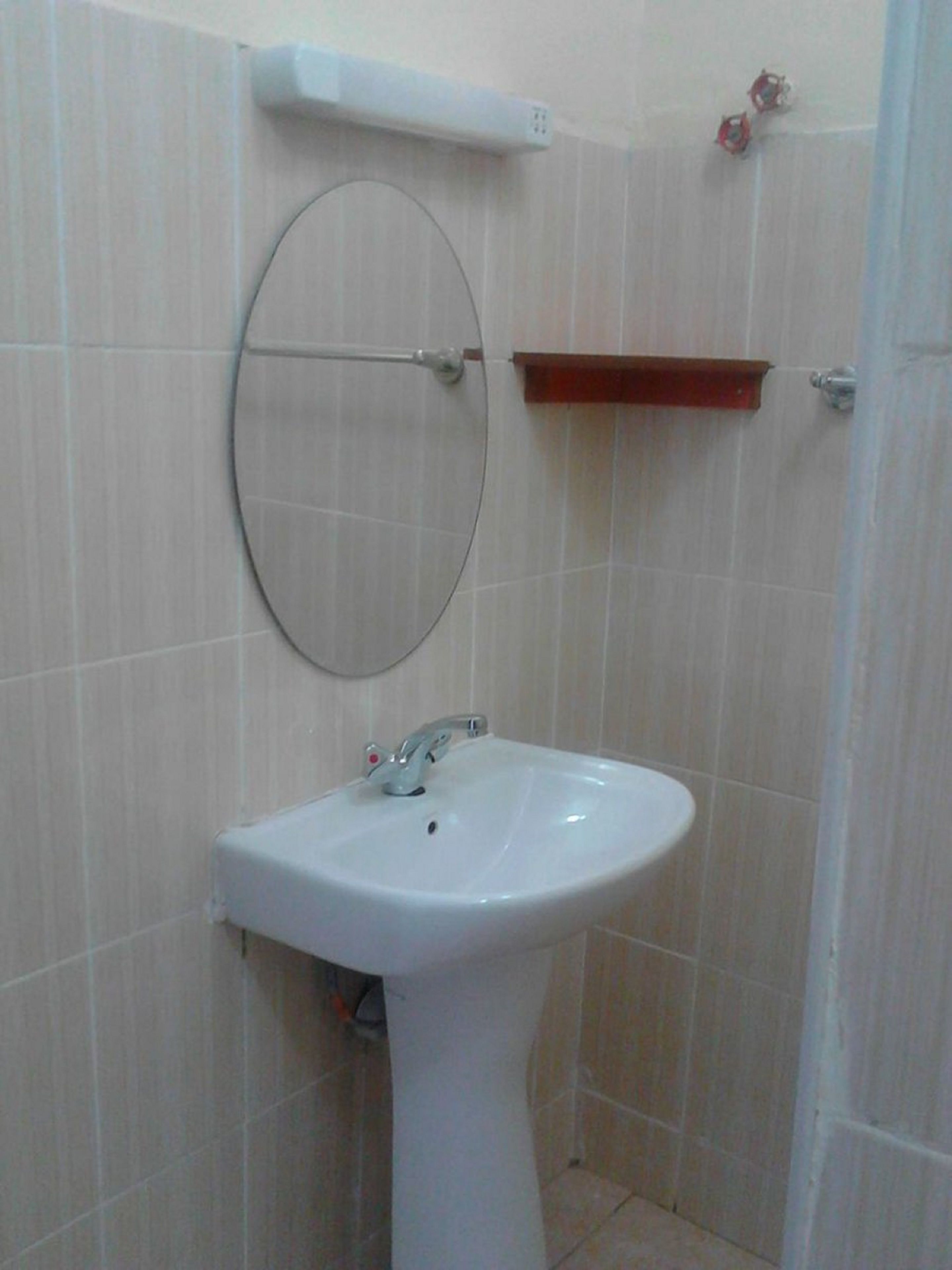 Un baño con un lavamanos blanco, un espejo y un estante rojo.