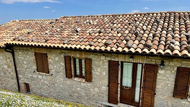 A stone building with a tiled roof, wooden shutters, and a small garden with white and yellow flowers. - La Fattoria dei Sibillini (Montemonaco)