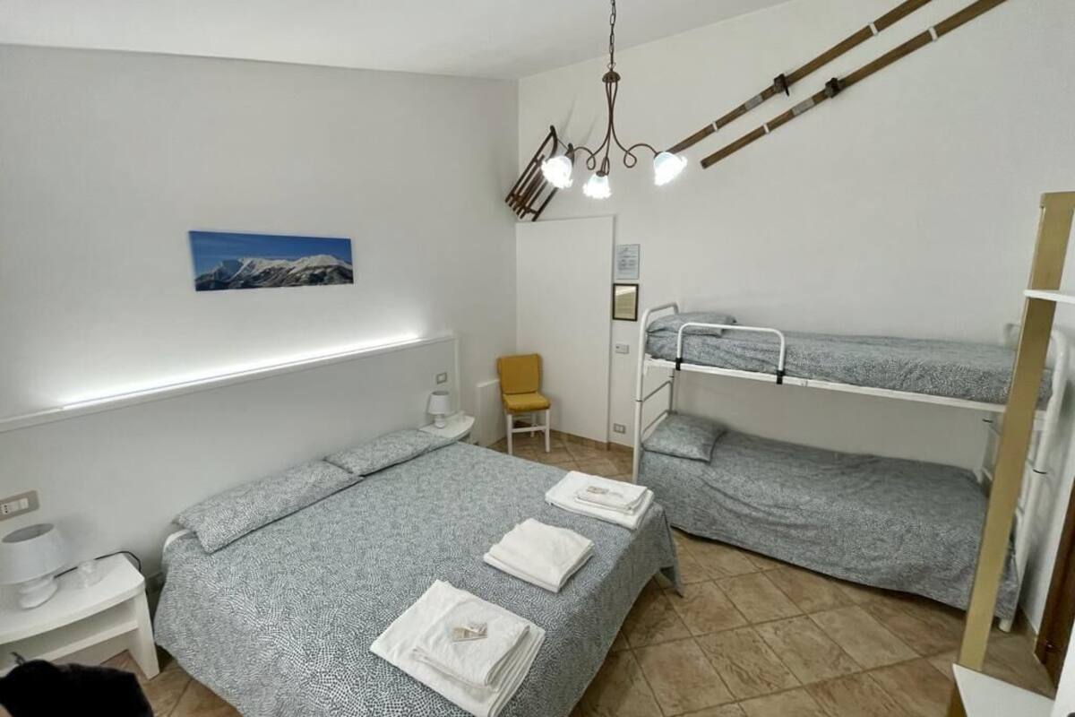 Een studentenkamer met stapelbedden, een bureau, een stoel, een lamp en een schilderij aan de muur.