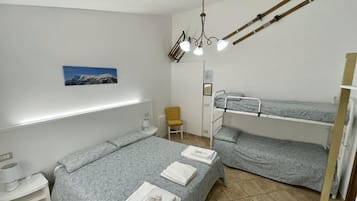 A dormitory room with bunk beds, a desk, a chair, a lamp, and a painting on the wall.