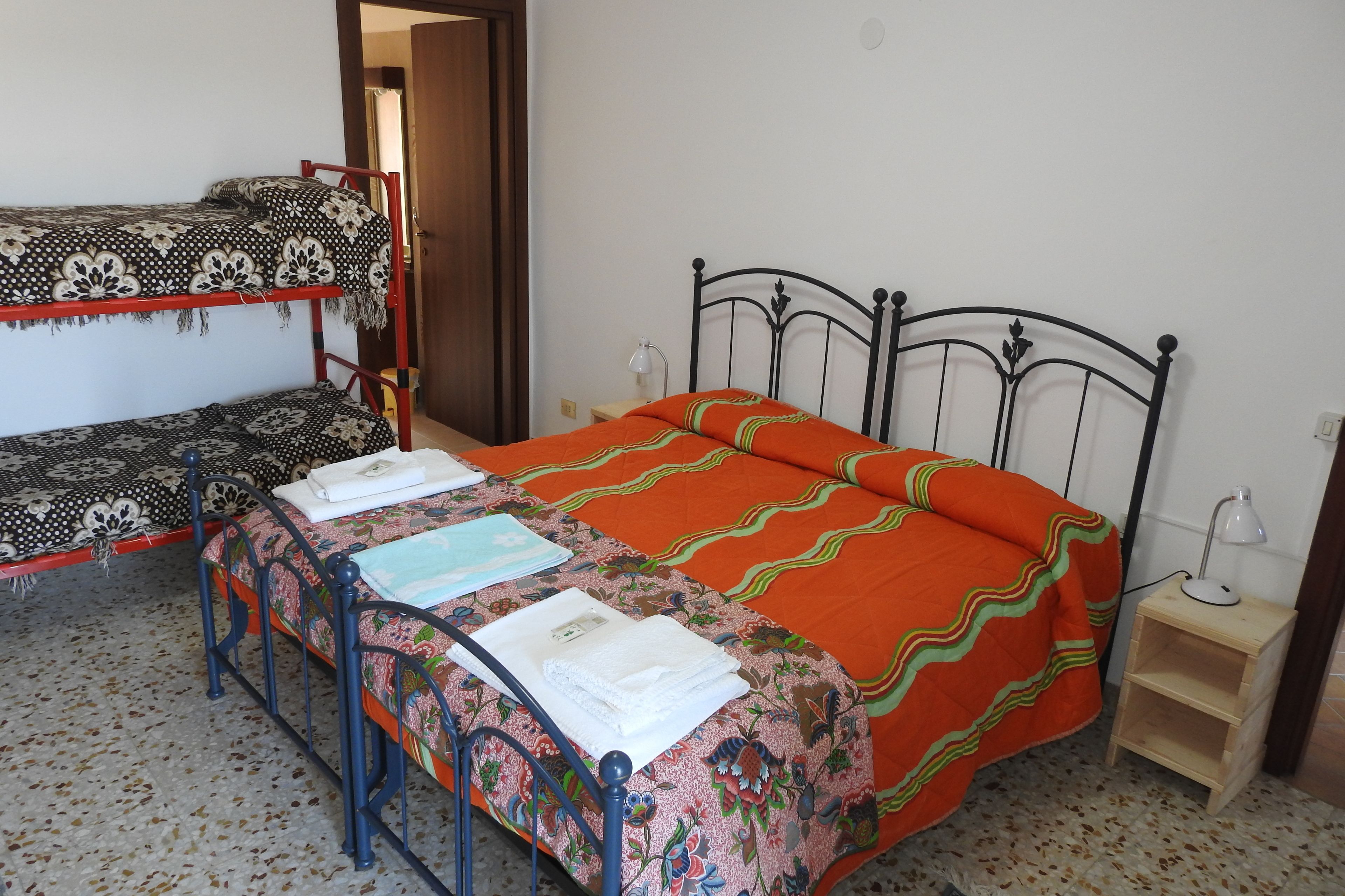 A dormitory room with two bunk beds, a single bed, and a small wooden nightstand with a lamp.
