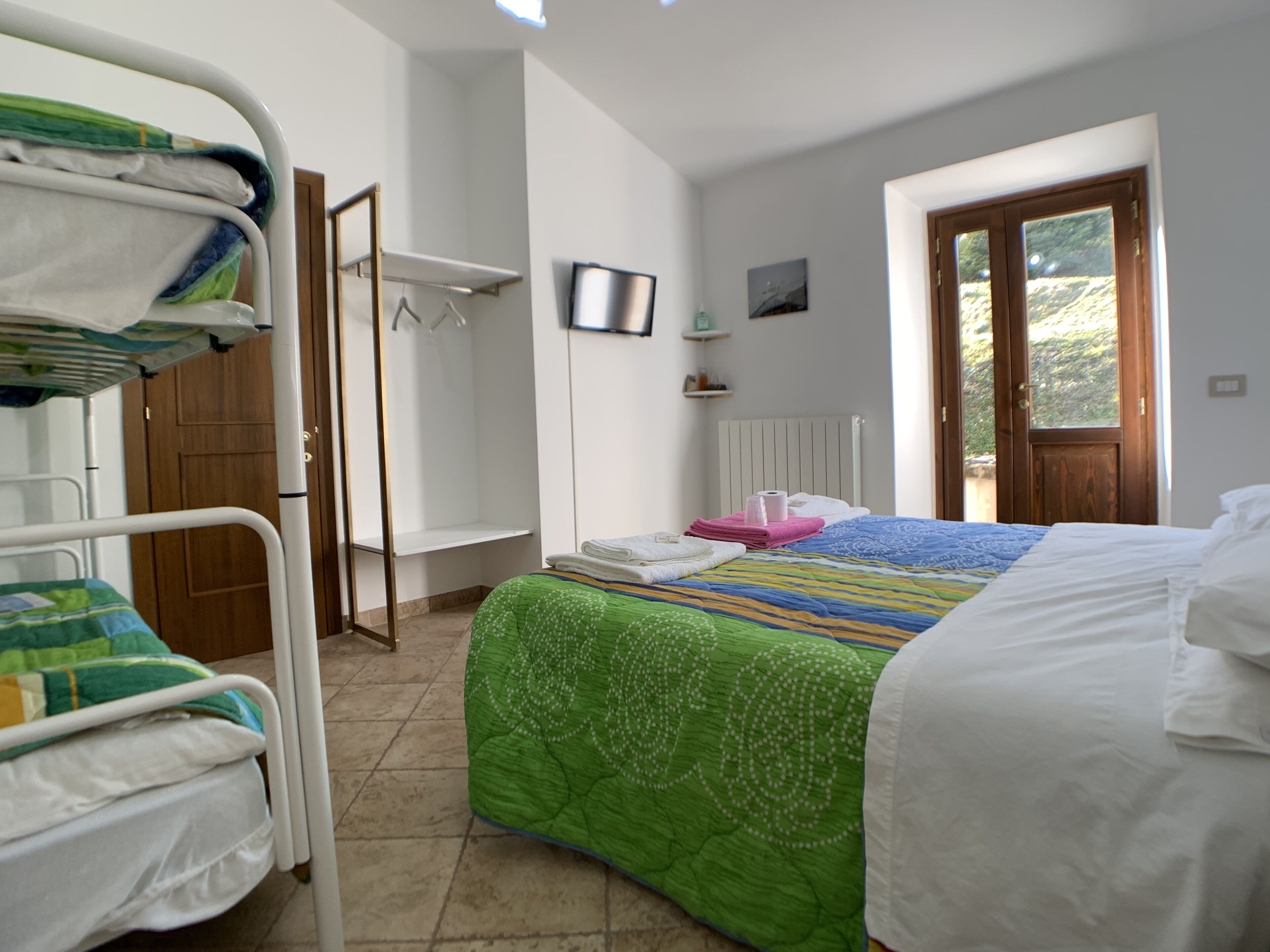 Quarto com beliches, uma cama de solteiro, radiador, televisão e porta para o exterior.