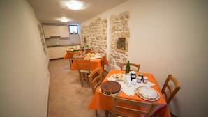 A dining area with a stone wall, wooden chairs, and a table set with food and drinks. - La Fattoria dei Sibillini (Montemonaco)