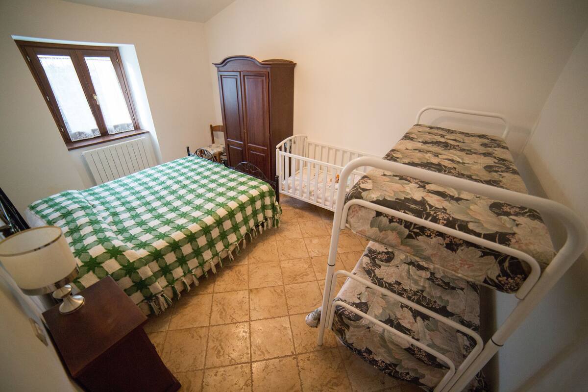 Een slaapkamer met een bed, een kinderbedje, een kledingkast, een radiator en een raam.