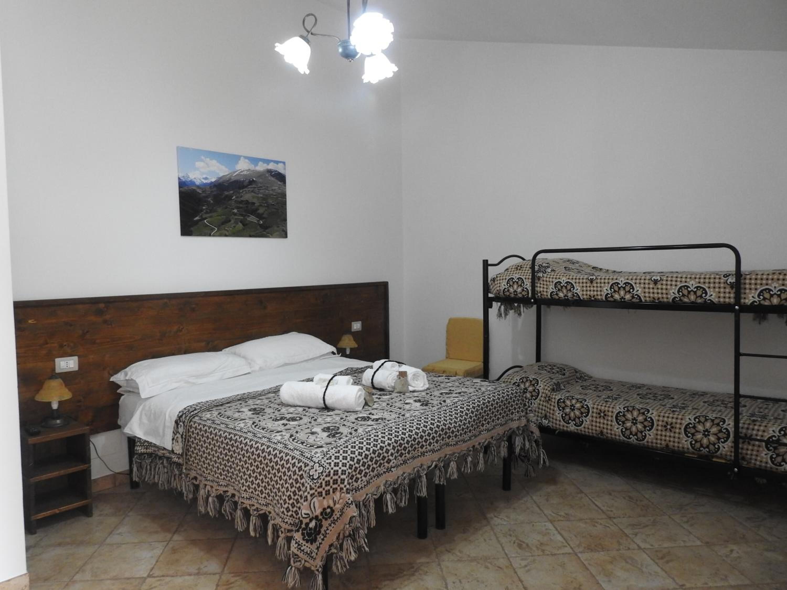 Een kamer met een houten bed, een stapelbed, een nachtkastje met een lamp en een foto van een berglandschap aan de muur.